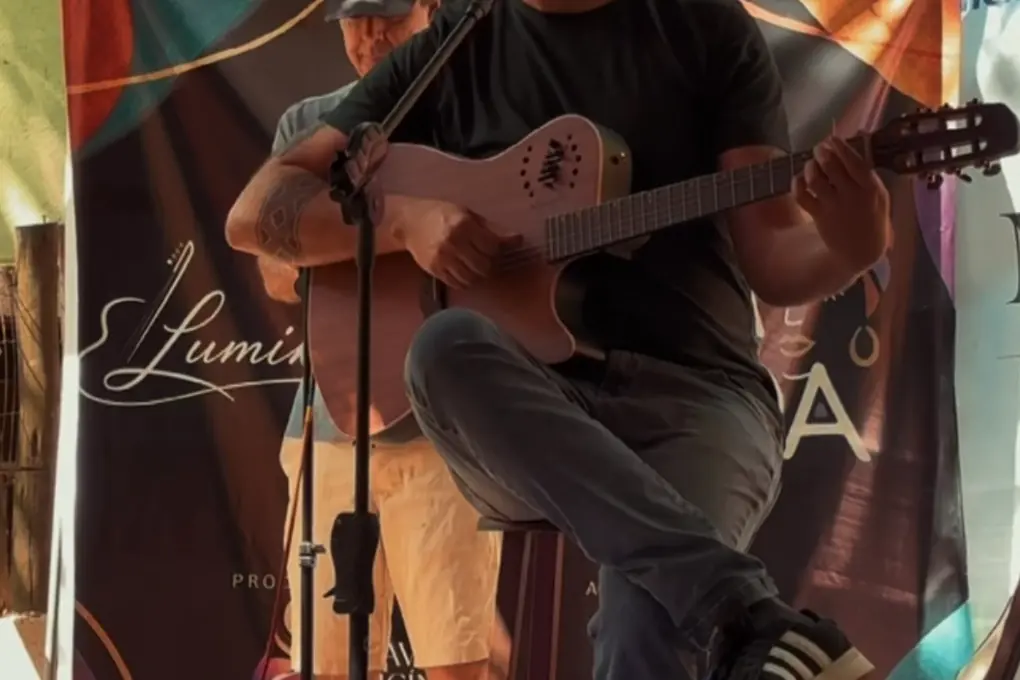 Músico tocando violão diante do banner do projeto